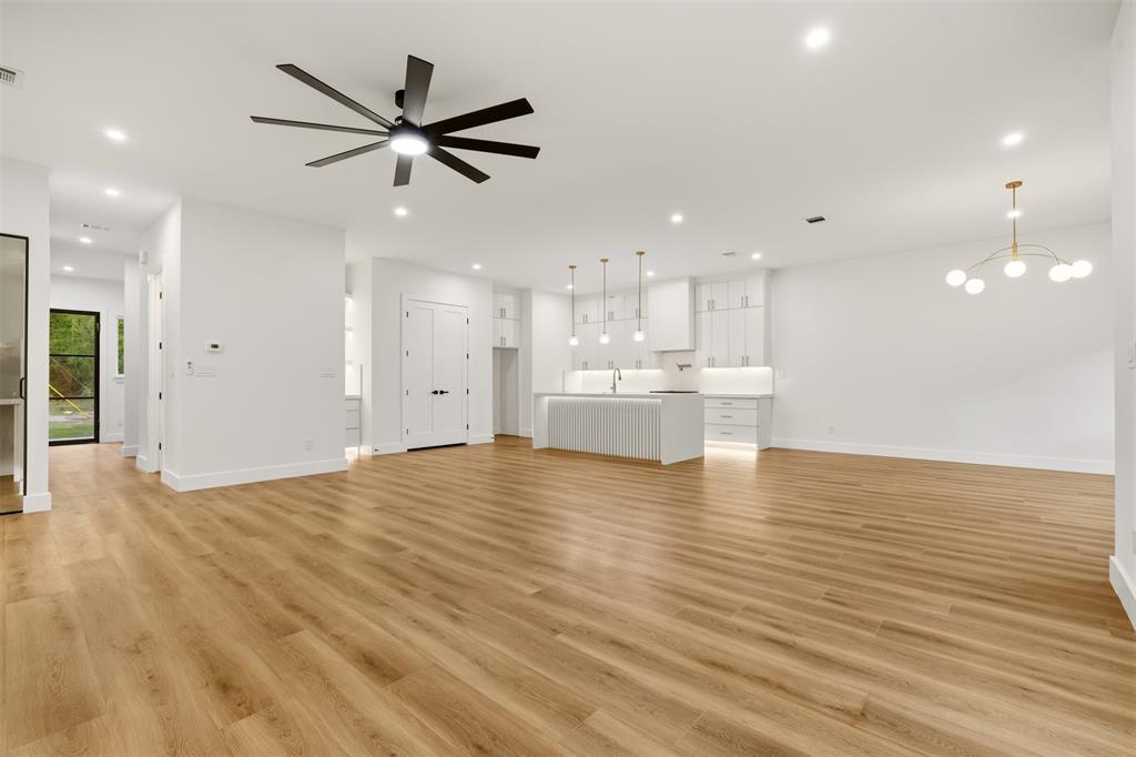 Open-concept interior featuring wood-finish flooring, a kitchen island with integrated lighting, flat-panel cabinetry, a multi-blade ceiling fan, and modern multi-globe chandelier lighting