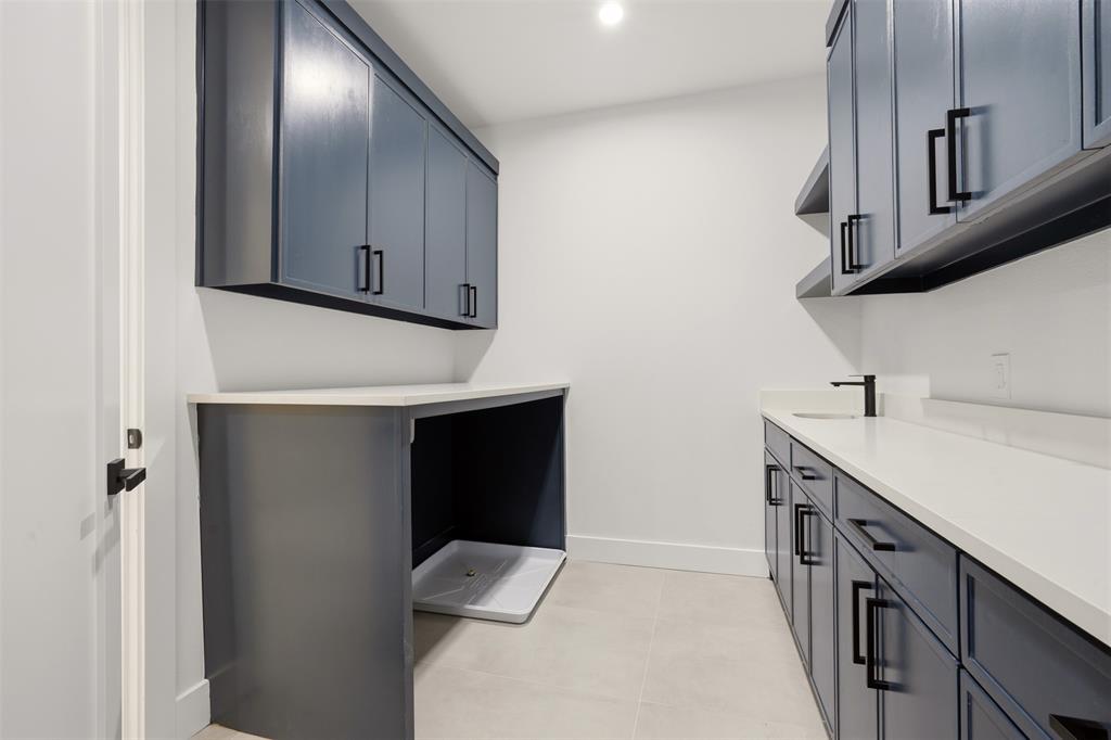 Blue cabinetry with matte black hardware, light-toned stone-finish countertops, tile flooring, built-in lower and upper storage, and a sink with a matte black faucet