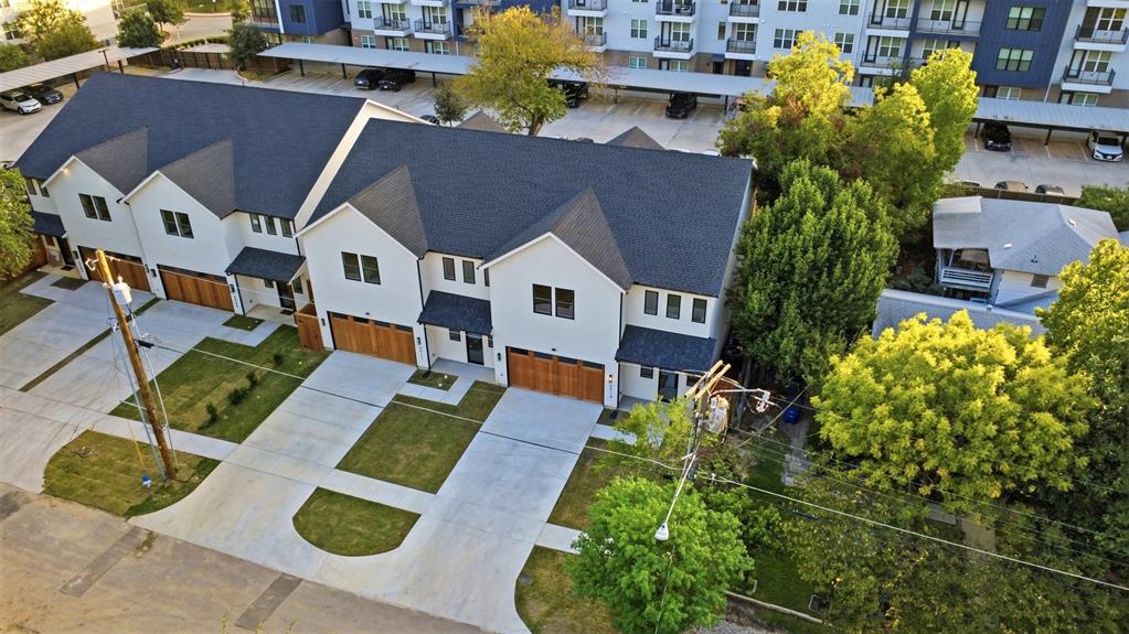 Multi-unit residential structure featuring a gable roof, white exterior siding, wooden garage doors, and individual concrete driveways