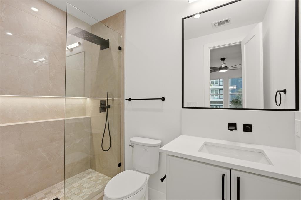 Walk-in shower with floor-to-ceiling tile, frameless glass enclosure, recessed wall niche, matte black rainfall showerhead, and floating vanity with an integrated sink and quartz countertop