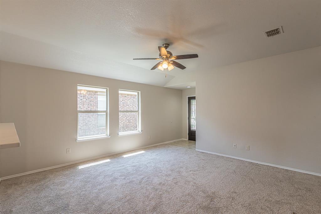 Carpeted room featuring light-colored walls, two double-hung windows, a ceiling fan with integrated lighting, and a dark-paneled door with decorative glass