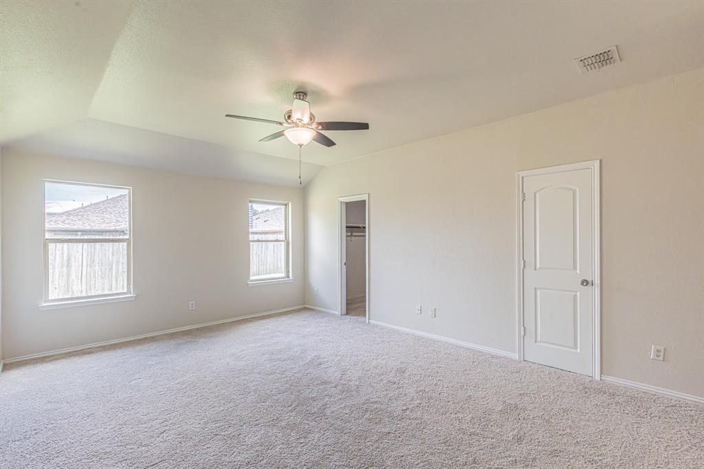 Spacious room featuring vaulted ceilings, light-colored carpeting, two windows with white trim, a ceiling fan with integrated lighting, and a walk-in closet
