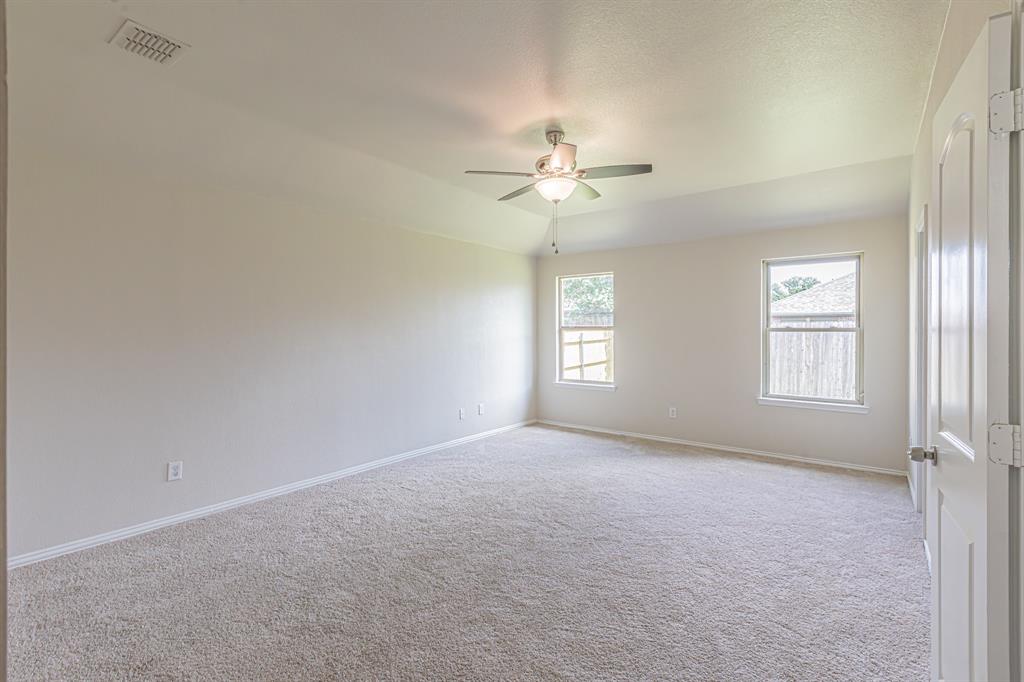 Spacious room featuring neutral carpeting, a ceiling fan with integrated lighting, two windows, and a tray ceiling