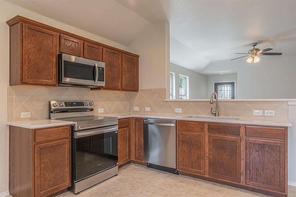 Kitchen featuring wood cabinetry, stainless steel appliances including an oven range and microwave, light-toned countertops, and a tiled backsplash