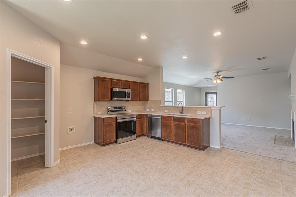 Open-concept kitchen featuring tile flooring, stainless steel appliances, wood-finish cabinetry, and a generously sized pantry
