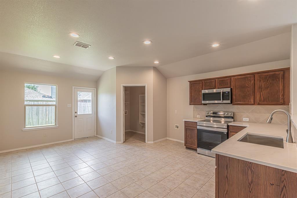 Kitchen area with tile flooring, wood-finish cabinetry, stainless steel appliances, and light-toned countertops