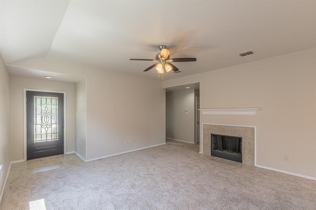 Spacious living area featuring a tile-surround fireplace with a classic mantel, ceiling fan, and carpet flooring