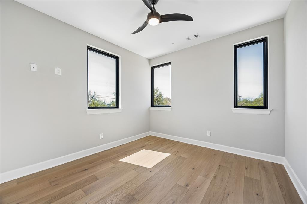 Room featuring wood-finish flooring, three black-framed windows, and a ceiling-mounted light fixture with a fan