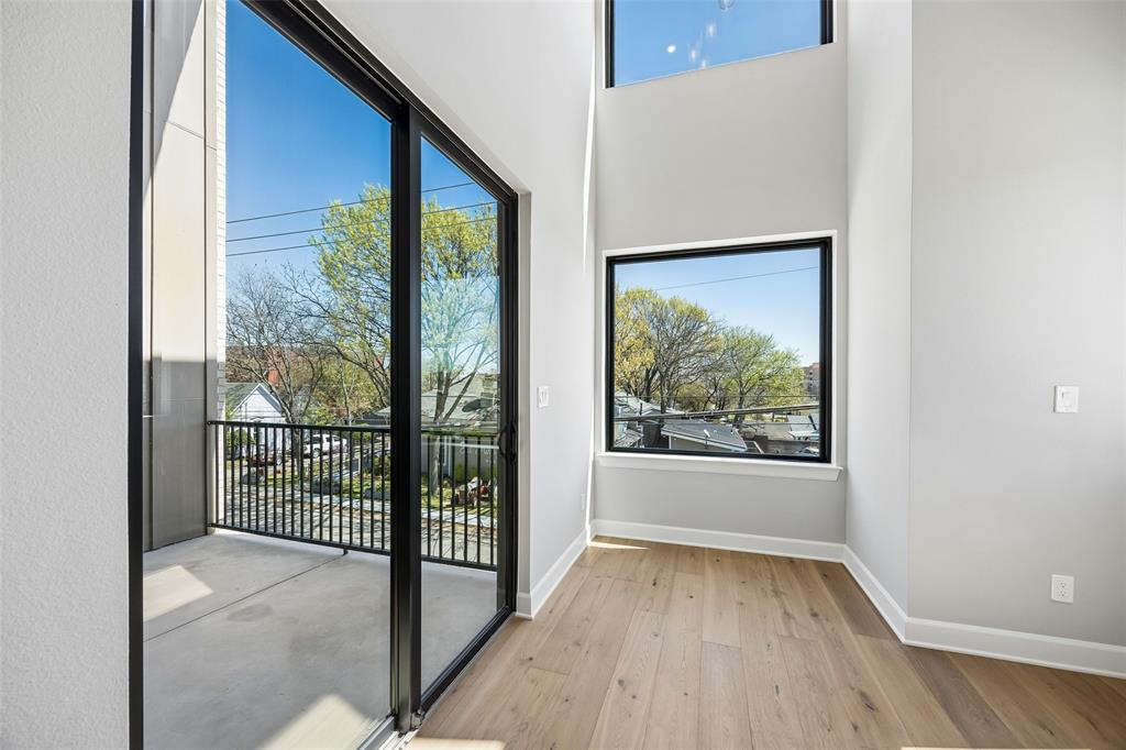 Double-height ceilings featuring expansive windows, wood-finish flooring, and a covered balcony with a black metal railing