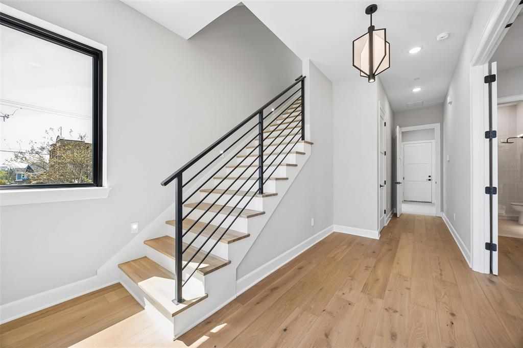 Staircase featuring wood-finish treads and a matte black metal railing, wide-plank wood-finish flooring, geometric pendant lighting, and large rectangular window with a black frame