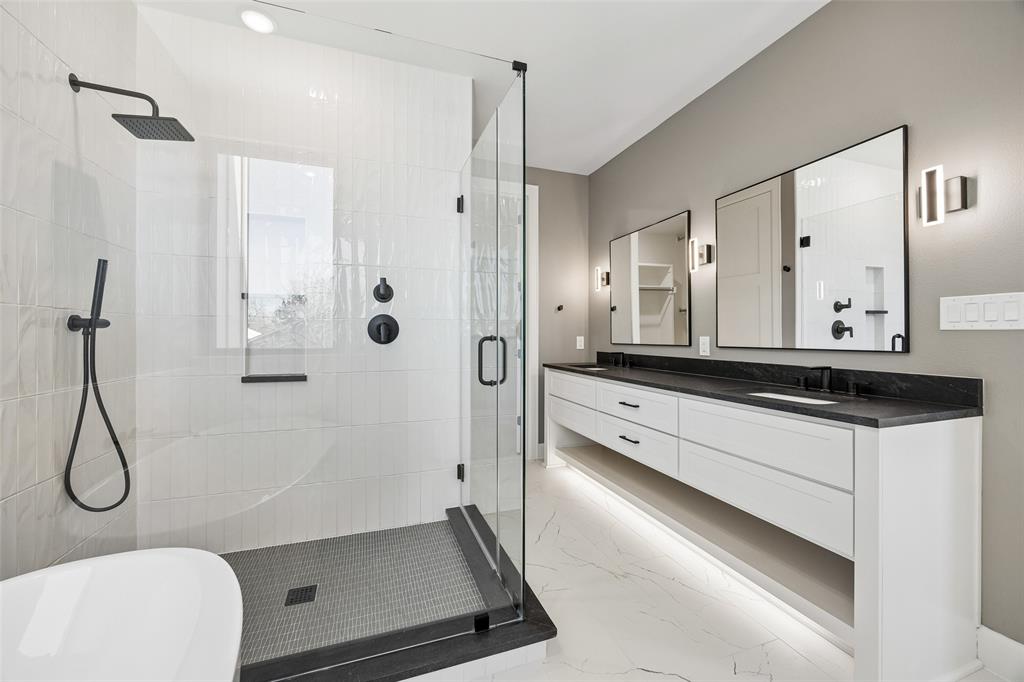 Floating double vanity with a dark countertop and integrated lighting, walk-in shower with a glass enclosure, matte black fixtures, and patterned tile flooring