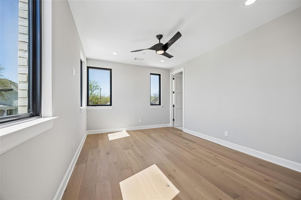 Neutral-toned room featuring wide-plank wood-finish flooring, recessed lighting, matte black ceiling fan, and large windows with black frames
