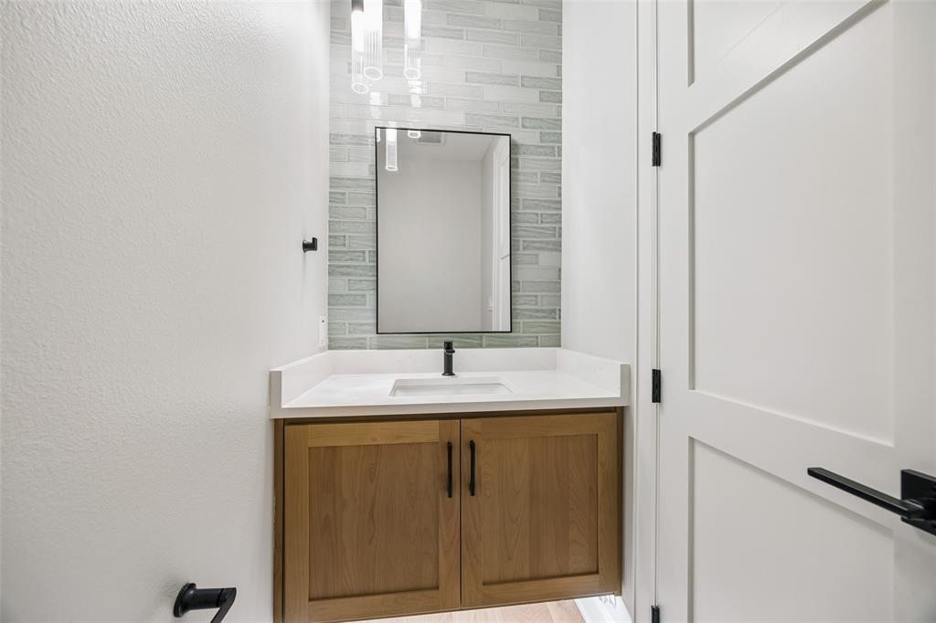 Floating wood-finish vanity with a white countertop, integrated rectangular sink, matte black hardware, and linear tile backsplash accented by a framed mirror and pendant lighting