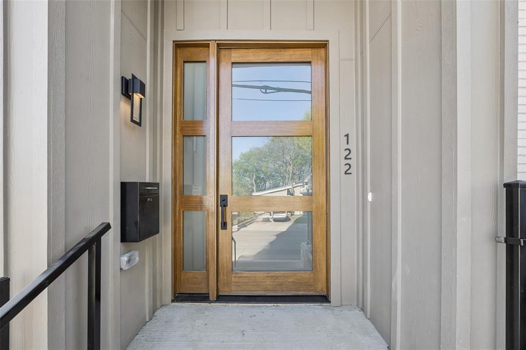 Modern wood-finish entry door with glass panels, rectangular side-light, matte black hardware, and wall-mounted exterior lighting