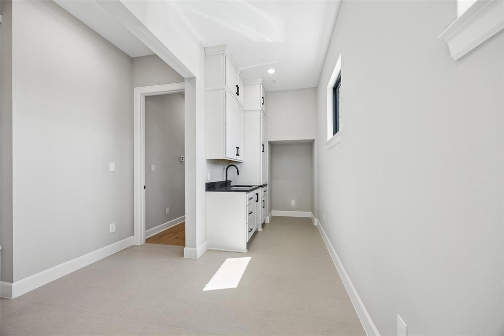 Built-in cabinetry with white finish, dark stone-style countertops, matte black faucet, and light tile flooring