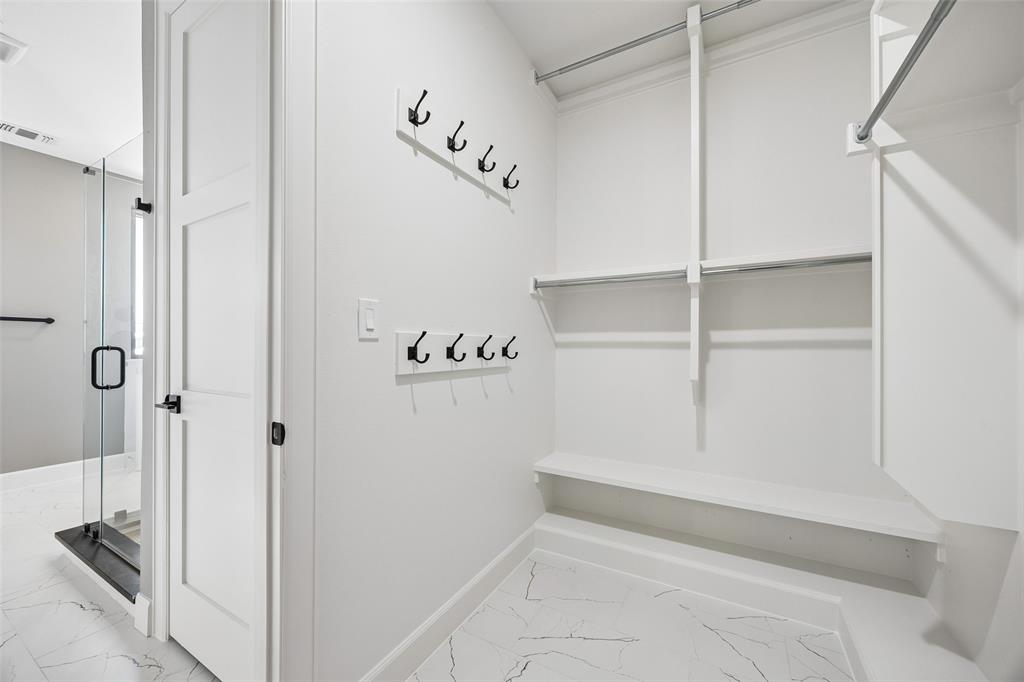 Walk-in closet featuring white built-in shelving, dual-tier hanging rods, two wall-mounted matte black hook racks, and large-format tile flooring with a veined pattern