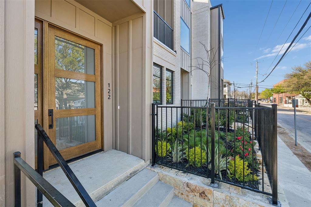 Modern exterior featuring a wood-panel door with glass inserts, vertical siding, stone masonry, a black metal fence, and landscaped shrubbery