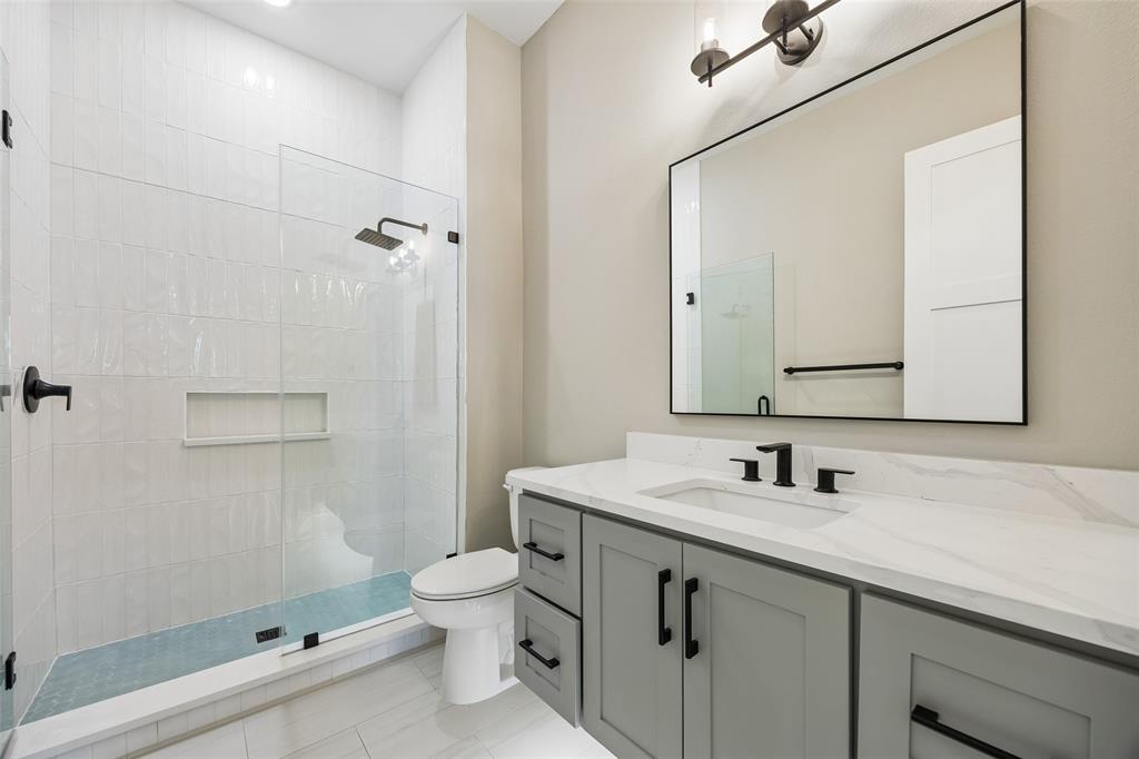 Bathroom featuring a vanity with a white countertop and rectangular undermount sink, matte black hardware, glass-enclosed shower with vertical tile surround and integrated niche, and a framed mirror