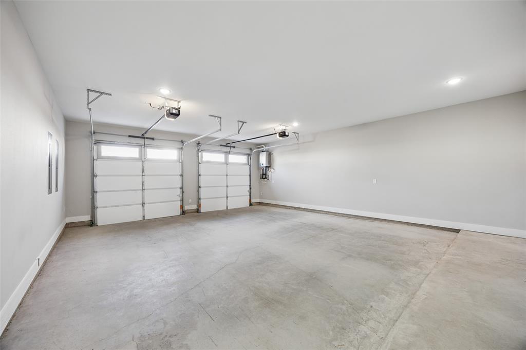 Three-car garage featuring finished walls, concrete flooring, dual automatic door openers, and a wall-mounted tankless water heater