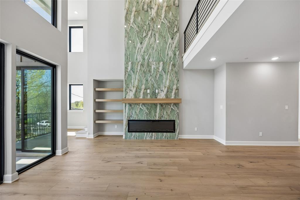 Double-height ceiling, floor-to-ceiling stone fireplace surround, linear built-in fireplace, wood-finish flooring, and minimalist floating shelving