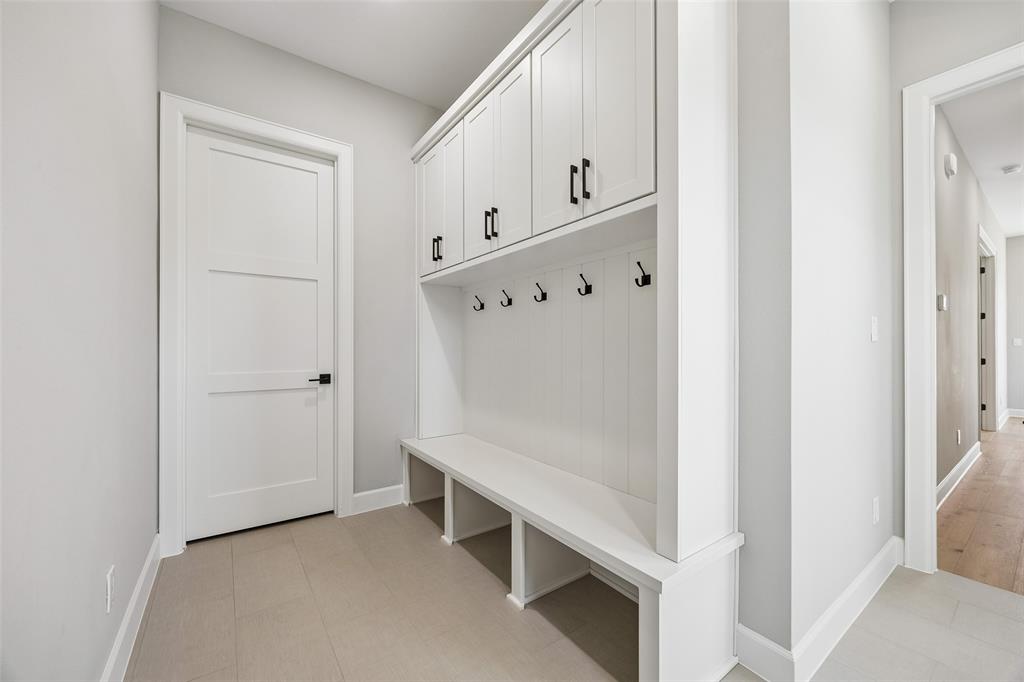 Custom built-in mudroom storage featuring white shaker-style cabinetry, open lower cubbies, a bench seat, and matte black hardware