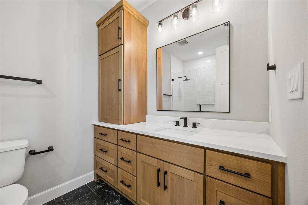 Bathroom featuring a light wood cabinetry vanity with a built-in tower, white countertop with an integrated rectangular sink, dark hardware, and black tile flooring