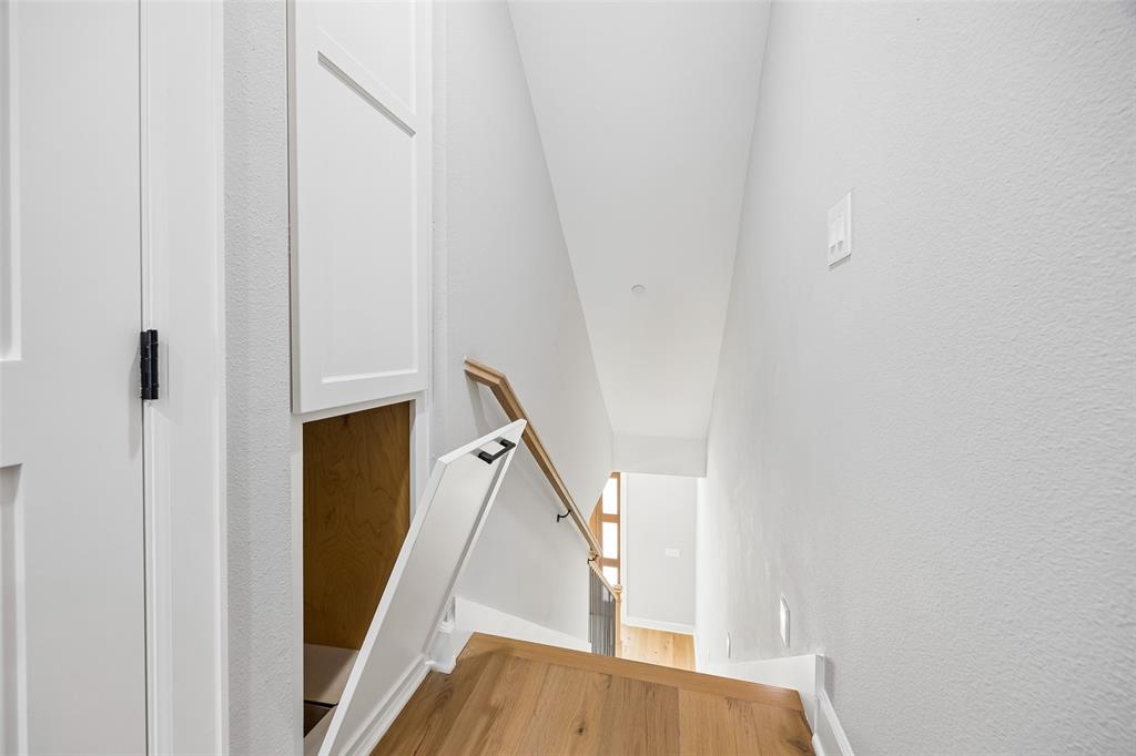 Staircase featuring wood-finish flooring, a wall-mounted wooden handrail, and built-in under-stair cabinetry with matte black hardware