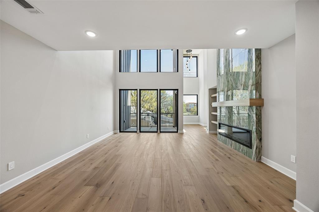 Two-story living area featuring wood-finish flooring, floor-to-ceiling stone fireplace surround with integrated hearth, built-in shelving, and expansive grid windows