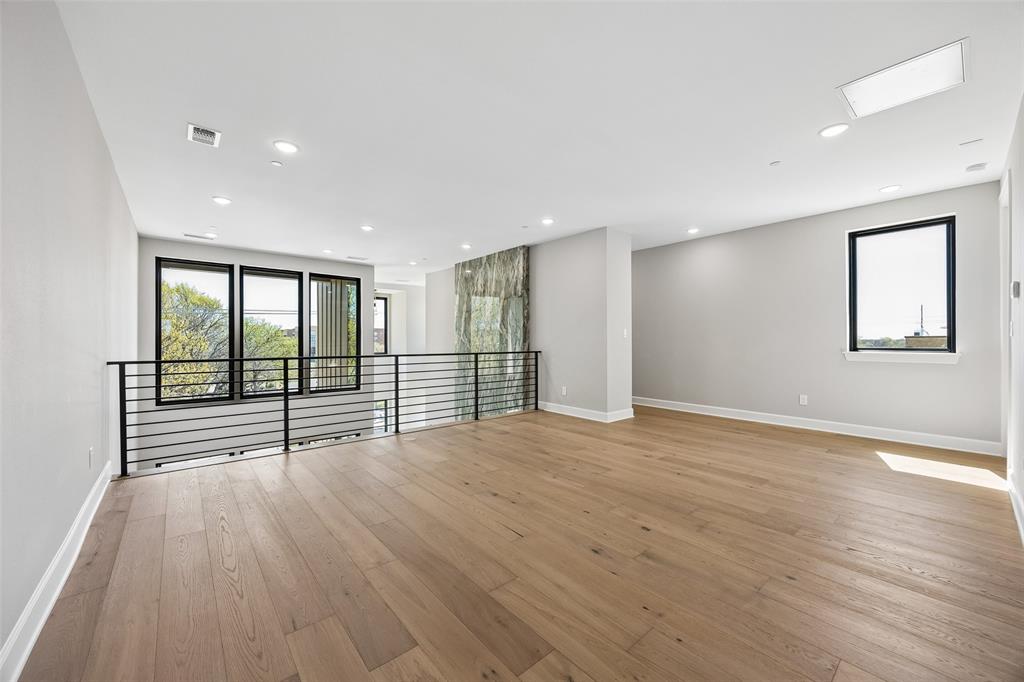Open-concept interior featuring light-toned wood-finish flooring, metal horizontal-bar railing, multiple large windows, and recessed lighting