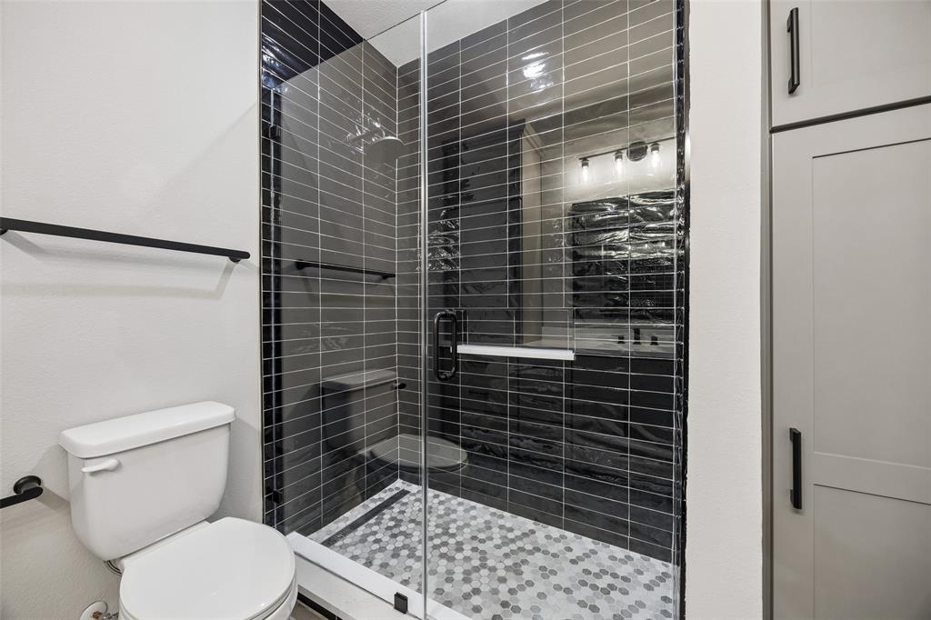 Walk-in shower featuring black subway tile surround, glass enclosure, hexagonal mosaic floor tile, and matte black hardware, accompanied by built-in floor-to-ceiling cabinetry