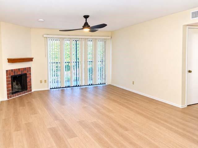 Corner fireplace with red brick surround and wooden mantel, wood-finish flooring, ceiling fan with integrated lighting, and sliding glass doors with vertical blinds Corner fireplace with red brick surround and wooden mantel, wood-finish flooring, ceiling fan with integrated lighting, and sliding glass doors with vertical blinds