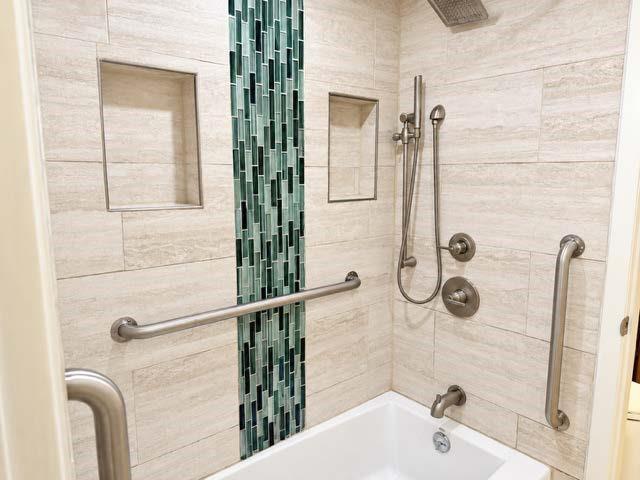 Shower enclosure featuring large-format neutral wall tile, a vertical decorative glass mosaic accent strip, two built-in recessed niches, brushed nickel plumbing fixtures, and integrated support bars