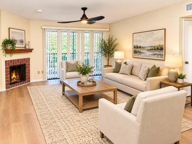 Staged Corner fireplace featuring a red brick surround and a wood mantel, wood-finish flooring, ceiling fan, and vertical blinds covering a large glass panel door Staged Corner fireplace featuring a red brick surround and a wood mantel, wood-finish flooring, ceiling fan, and vertical blinds covering a large glass panel door