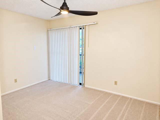 Room featuring neutral carpeting, a ceiling fan with integrated lighting, and sliding glass doors with vertical blinds