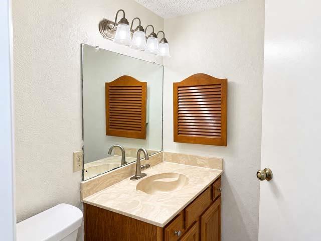 Vanity featuring a light-toned solid surface countertop with an integrated oval sink, wood-finish cabinetry, a wall-mounted louvered storage cabinet, and a four-light brushed-finish vanity fixture