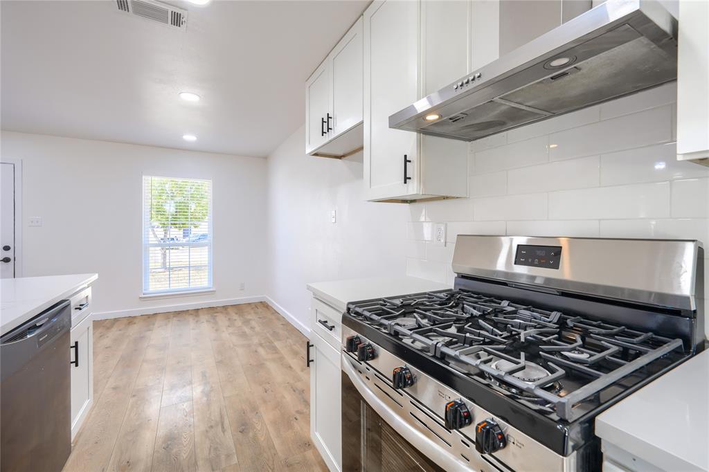 Kitchen featuring white shaker-style cabinetry, quartz countertops, subway tile backsplash, stainless steel gas range with overhead vent hood, and wood-finish flooring