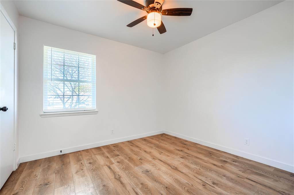 Neutral-toned room featuring wood-finish flooring, a ceiling fan with integrated lighting, and a single-pane window