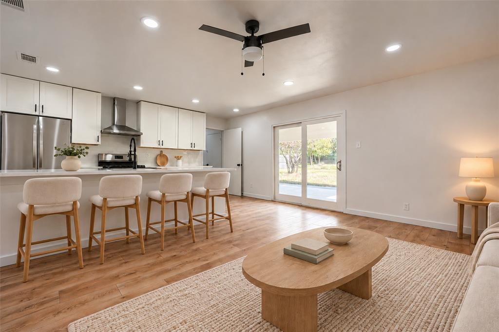 Kitchen featuring white shaker cabinetry, stainless steel appliances, a center island with a breakfast bar, recessed lighting, and wood-finish flooring throughout the open-concept space