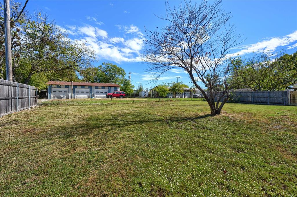 Expansive open lot featuring a perimeter wood fence, grass terrain, and mature trees