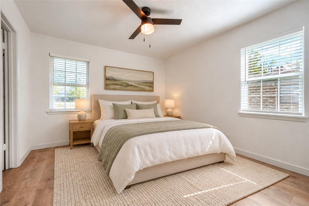 Neutral-toned room featuring wood-finish flooring, two windows with horizontal blinds, and a ceiling-mounted light fixture with an integrated fan