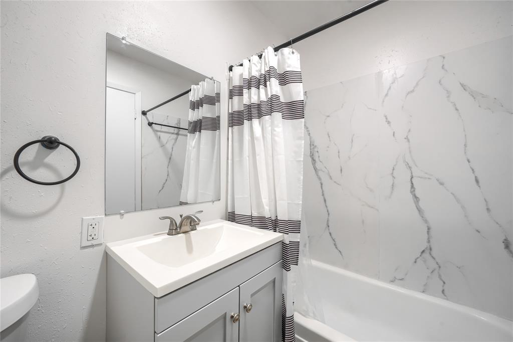 Bathroom featuring a vanity with a light-colored countertop, integrated sink basin, and neutral-toned cabinetry, complemented by a bathtub with wall panels featuring a veined finish and a wall-mounted mirror
