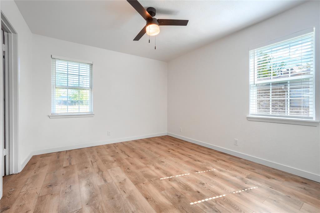 Neutral-toned interior featuring wood-finish flooring, two windows with horizontal blinds, and a dark-finish ceiling fan with an integrated light fixture