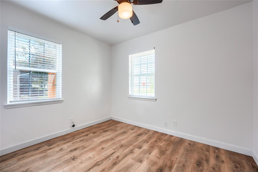 Room featuring wood-finish flooring, two windows with horizontal blinds, and a ceiling-mounted light fixture with a fan