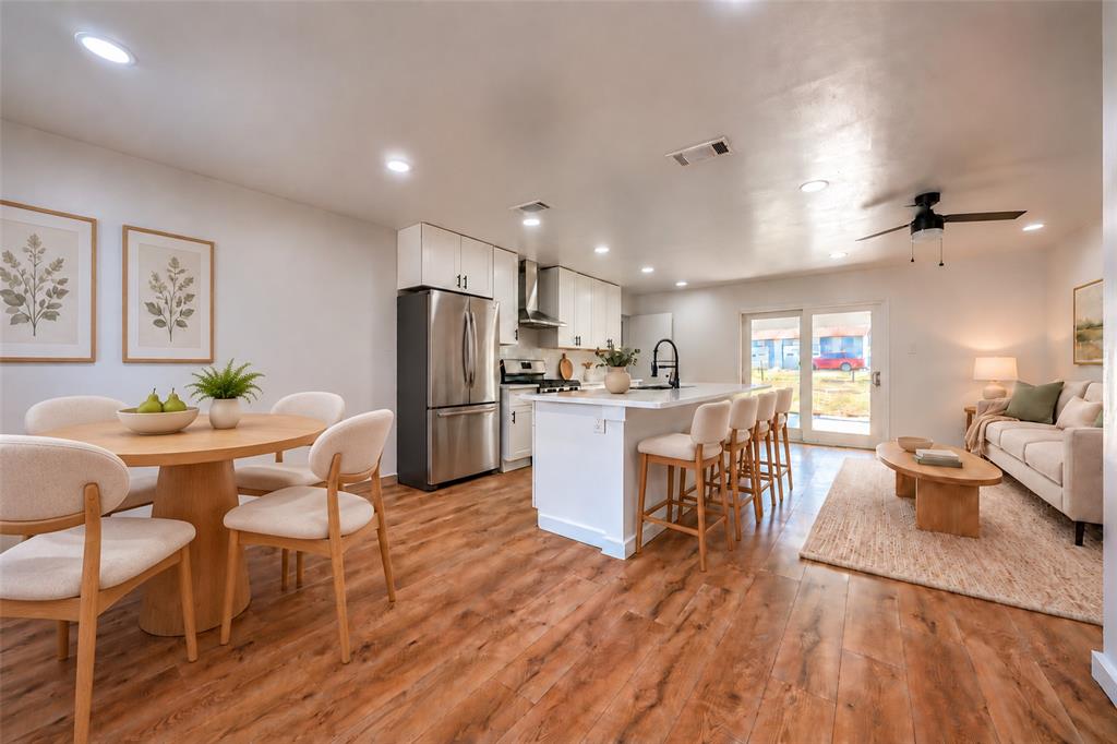 Open-concept area featuring wood-finish flooring, white cabinetry, a center kitchen island with bar seating, stainless steel appliances, and recessed lighting