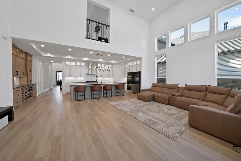 Double-height living area featuring floor-to-ceiling windows, wood-finish flooring, a kitchen island with seating, built-in cabinetry, and a mezzanine overlook with metal railing