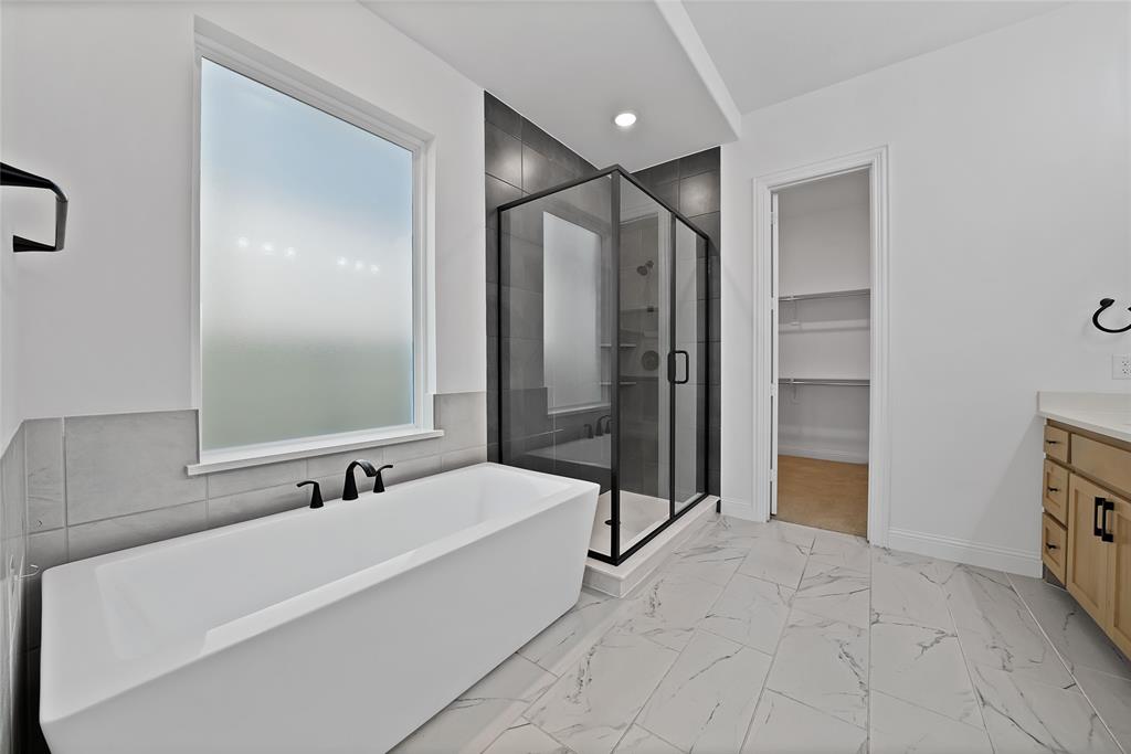 Freestanding soaking tub with matte black fixtures, walk-in shower featuring dark tile surround and glass enclosure, tile flooring, light wood cabinetry, and recessed lighting