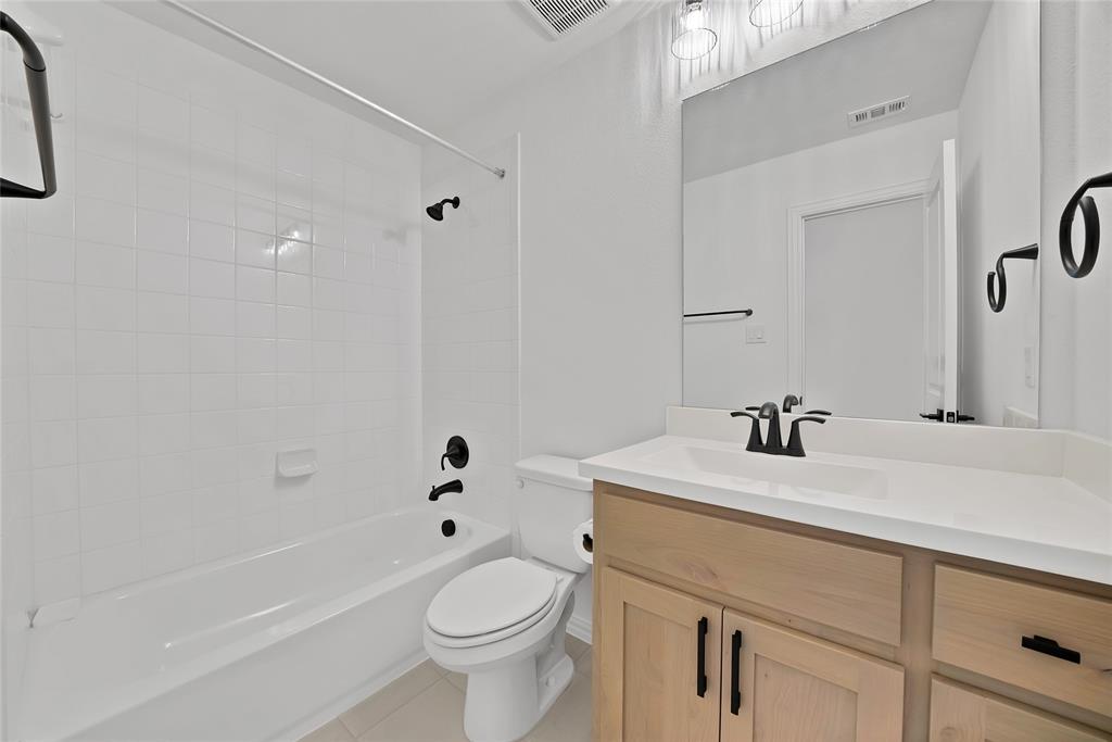 Bathroom featuring a light wood-finish vanity with a white integrated sink, matte black hardware, a large wall-mounted mirror, and a tub-shower combination with square wall tile