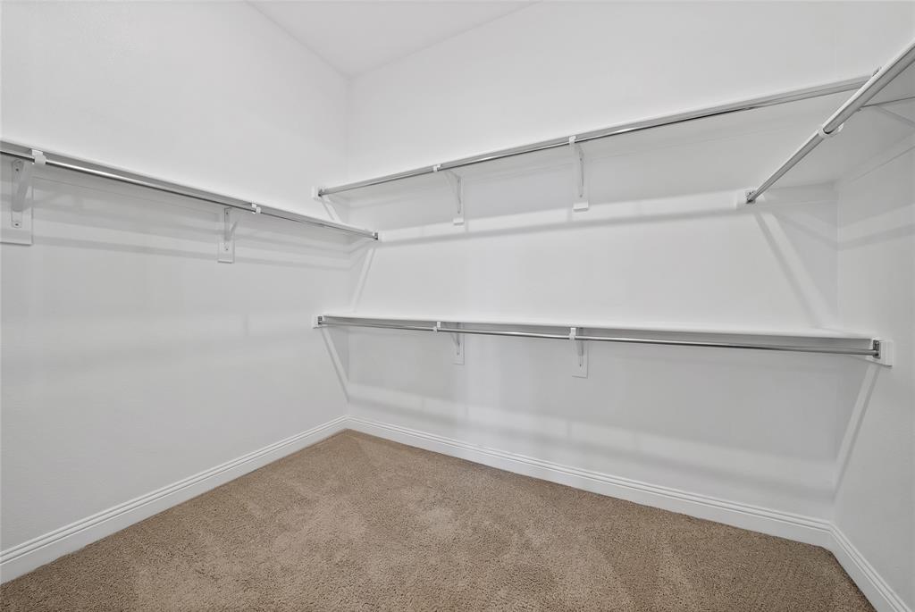 Walk-in closet featuring neutral carpeting and tiered metal shelving units with integrated garment rods