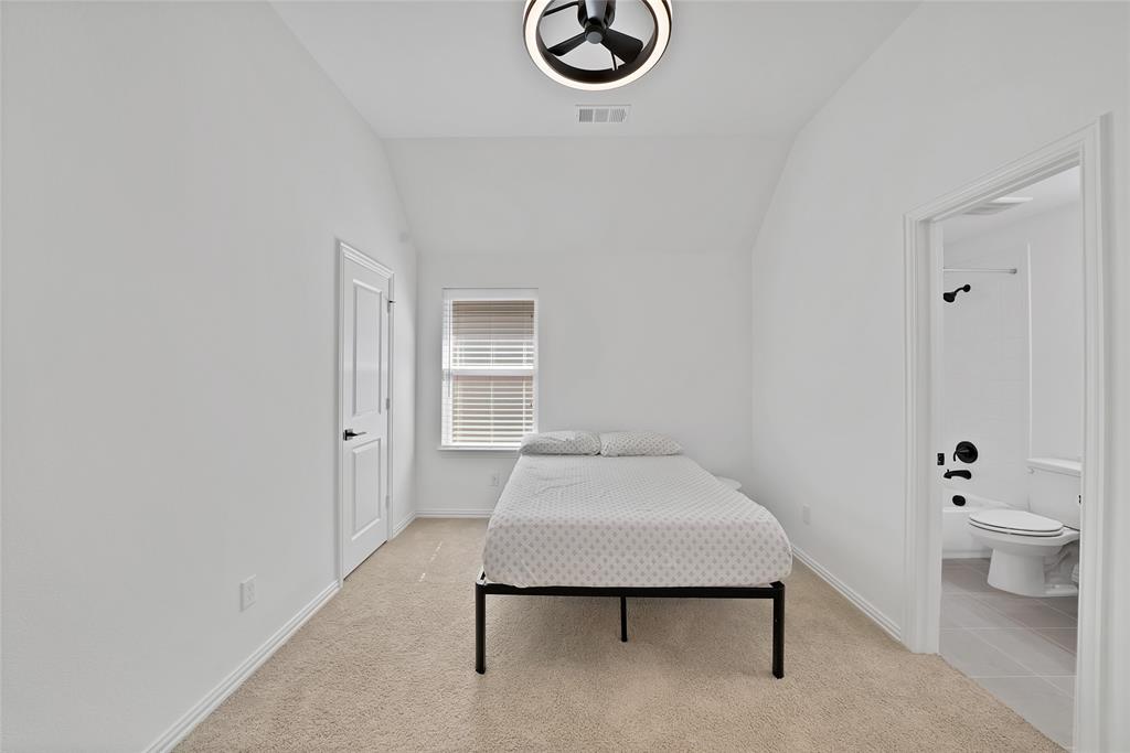 Vaulted ceiling featuring a contemporary circular flush-mount light fixture, neutral wall-to-wall carpeting, and a private bath entry