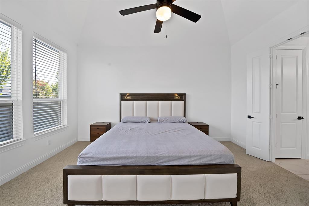 Vaulted ceiling with an integrated matte black ceiling fan, dual windows with horizontal blinds, neutral wall-to-wall carpeting, and paneled doors with matte black hardware